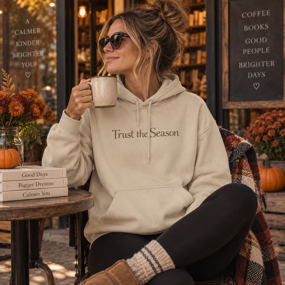 Model wearing the Trust the Season hoodie in a cozy autumn coffee and bookstore setting